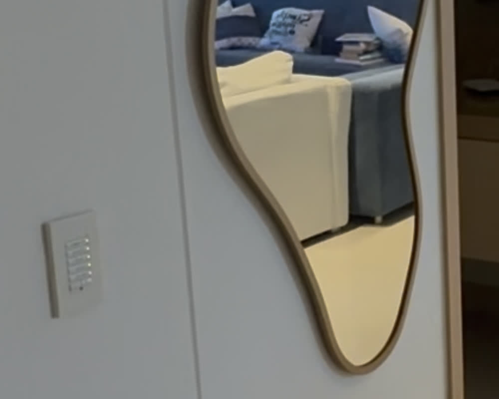 Acceso a la sala principal: la botonera está montada en la pared blanca, junto al espejo ondulado que refleja los sofás de la sala